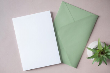 Empty white blank greeting or invitation card, green envelope, cactus on beige background.