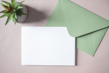 Empty white blank greeting or invitation card, green envelope, cactus on beige background.
