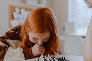 A teenage girl and her mother play chess in a bright living room, sharing an authentic moment of family bonding and strategic fun. Real photography capturing genuine connection