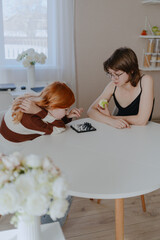 A teenage girl and her mother play chess in a bright living room, sharing an authentic moment of family bonding and strategic fun. Real photography capturing genuine connection