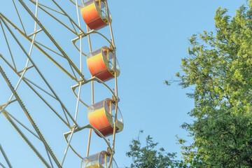 Ferris Wheel And Green Trees Against Blue Sky. Summer Amusement Park Scene With Ferris Wheel Rising Above Lush Foliage And Sunlight.