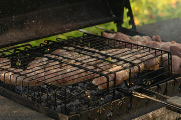 Grilled sausages cooking over hot charcoal on outdoor barbecue. Outdoor grilling of fresh sausages on charcoal barbecue with smoke heat and summer garden background.