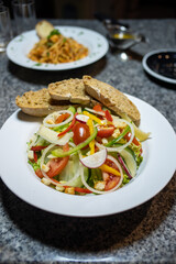 fresh vegetable salad served with slices of bread on a white plate. The salad contains tomato, cucumber, bell pepper, onion, radish, lettuce and croutons 