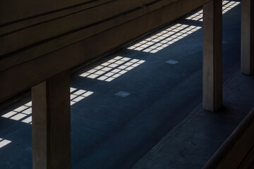 Sunlit grid shadows across concrete floor form geometric pattern between pillars in quiet modern space