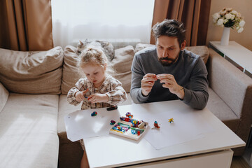 A 3-year-old girl and her father play with modeling clay in a sunny living room. Unfiltered,...