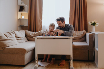 A 3-year-old girl and her father play with modeling clay in a sunny living room. Unfiltered,...