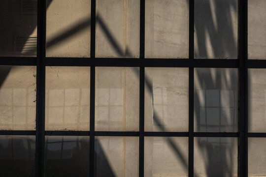 Abstract view large window panes forming grid with dark frames and dramatic shadows creating geometric light and texture across concrete surfaces