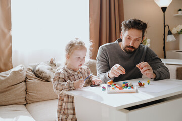 A 3-year-old girl and her father play with modeling clay in a sunny living room. Unfiltered,...
