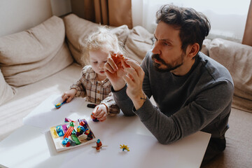 A 3-year-old girl and her father play with modeling clay in a sunny living room. Unfiltered,...