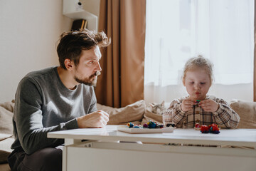 A 3-year-old girl and her father play with modeling clay in a sunny living room. Unfiltered,...