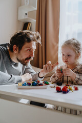 Obraz premium A 3-year-old girl and her father play with modeling clay in a sunny living room. Unfiltered, authentic photography capturing real family moments of creativity and bonding