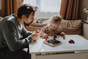 A 3-year-old girl and her father play with modeling clay in a sunny living room. Unfiltered,...