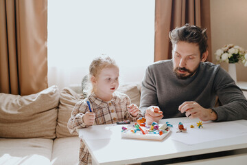 A 3-year-old girl and her father play with modeling clay in a sunny living room. Unfiltered,...