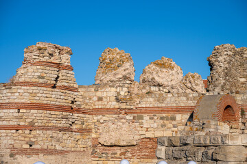 Ancient stone wall with red brick accents and weathered battlements stands beneath a clear blue sky in Nesebar, Bulgaria