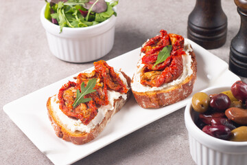 Two bruschettas with dried tomatoes, ricotta cheese and rucola on ciabatta bread. 