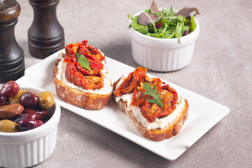 Two bruschettas with dried tomatoes, ricotta cheese and rucola on ciabatta bread. 