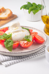 Traditional Italian burrata cheese with salad of delicious cherry tomato, basil leaves and olive oil.