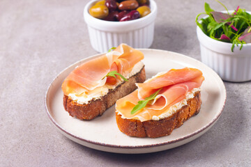 Two bruschettas with prosciutto, ricotta cheese and rucola on ciabatta bread. Olive and spices  decorated.