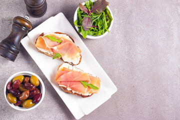 Two bruschettas with prosciutto, ricotta cheese and rucola on ciabatta bread. Olive and spices  decorated.