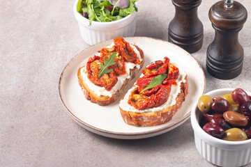 Two bruschettas with dried tomatoes, ricotta cheese and rucola on ciabatta bread. 
