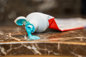A tube of blue toothpaste with the cap open and paste dripping onto a marble bathroom countertop