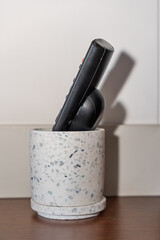 Close-up of two black TV remote controls placed upright inside a white terrazzo-style cup on a wooden surface