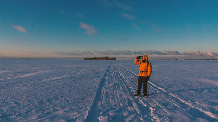 Explorer in orange jacket stands on snowy path under vast blue sky © darkbird