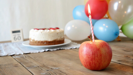 A shiny apple with a lit candle symbolizes a unique birthday celebration in a minimal white backdrop.