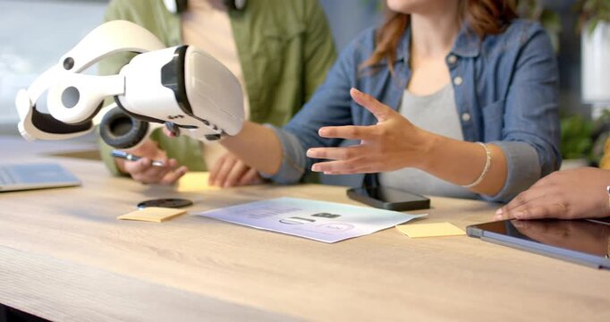 Diverse coworkers reacting to printer and inspecting VR headset at meeting table for design review