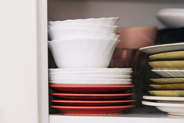 Kitchen cupboard with plates and bowls. Stacked dishes in different colors. Household tableware storage concept. Daily lifestyle in home interior. Organization of utensils indoors.