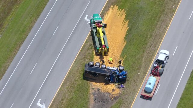 Overturned freight truck blocking road median with cargo of grain scattered across asphalt. Aerial view.