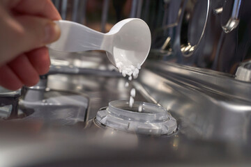 Hand pouring dishwasher salt into dispenser inside open dishwasher close up.