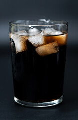 Close-up shot of dark brown soda with ice cubes in a clear glass against a black background. A refreshing and fizzy beverage, perfect for a cold, sweet treat