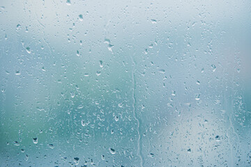Close up of raindrops on a glass window pane, featuring a blurred green background creating an abstract, natural scene. The water drops add texture and detail