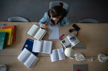 Female student  studying in library. Top view of working space with books and notes.