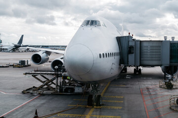 Obraz premium Large commercial airplane parked at airport gate, showcasing front view with jet bridge attached, surrounded by other aircraft and cloudy sky, illustrating air travel experience