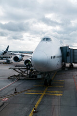 Large commercial airplane parked at airport terminal, with cargo loading equipment nearby, under a cloudy sky, showcasing aviation and transportation industry dynamics
