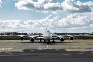 Large commercial airplane parked on airport runway, showcasing its sleek design and powerful engines, with a backdrop of clouds and blue sky, symbolizing air travel and aviation