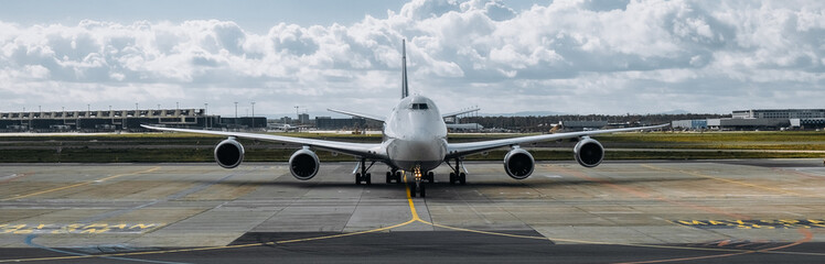 Fototapeta premium Large commercial airplane parked on runway, showcasing sleek design and powerful engines, with airport terminal and cloudy sky in the background, symbolizing air travel and aviation