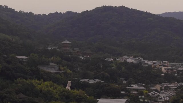 Serene aerial pan of Kyoto, Japan, featuring a forested hillside, Kiyomizu dera Temple, and traditional architecture in soft morning or evening light.
