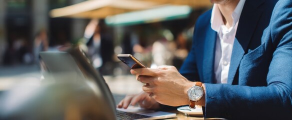 The businessman using smartphone at outdoor cafe with laptop and coffee