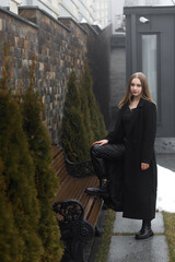 A young girl in a black coat and leather pants in a park in winter
