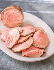 Perfectly sliced roast beef medium rare with seared crust on white plate