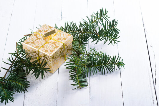 golden gift box and pine branches on white wood background