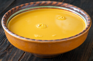 Creamy bisque served in clay bowl placed on rustic wooden table