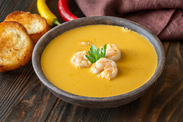 Rustic shrimp bisque with toasted baguette slices beside clay bowl