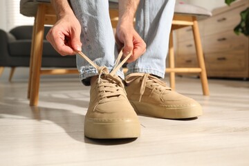 Man tying shoelace of beige sneaker indoors, closeup