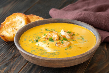 Rustic shrimp bisque with toasted baguette slices beside clay bowl