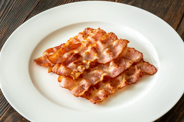 Crispy fried bacon slices neatly arranged on simple white serving plate