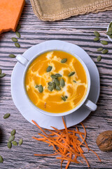 Pumpkin cream soup served with seeds and walnuts on rustic wooden table, traditional autumn dish and healthy seasonal comfort food